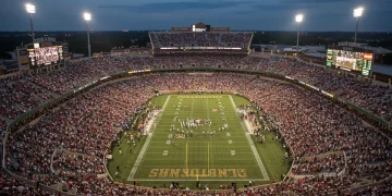 Packed college football stadium at night with bright lights and cheering fans, illustrating the sport's economic power.